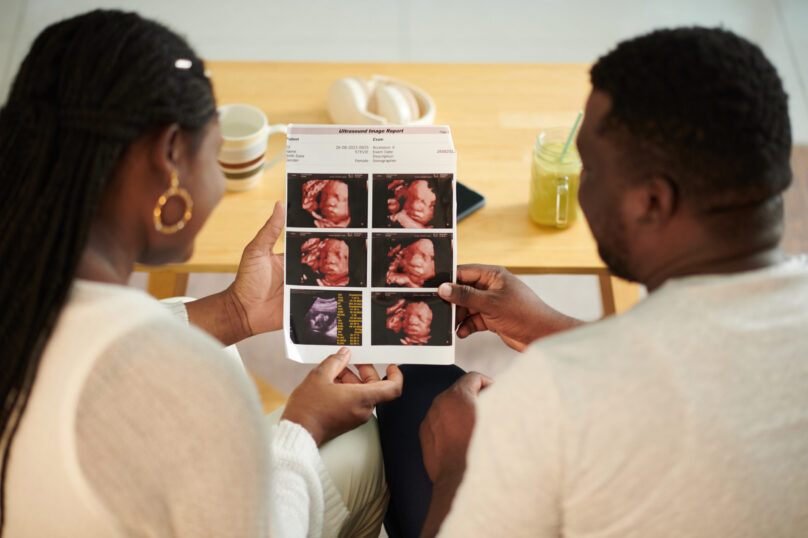 Pregnant woman showing ultrasound image of baby to husband, view over shoulder